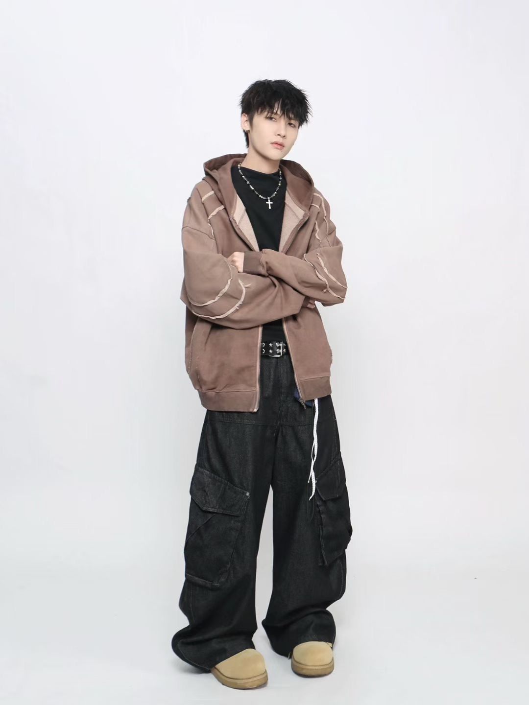 Person wearing a brown hoodie and black pants on a white background